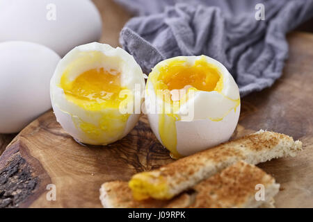 Due uova sode con toast soldati contro un sfondo rustico. Estrema profondità di campo con il fuoco selettivo sul tuorlo. Foto Stock