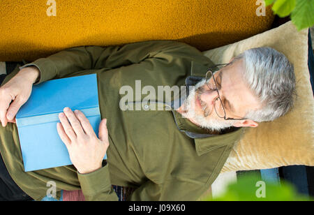 Uomo dorme con un libro su un divano letto in cantiere Foto Stock