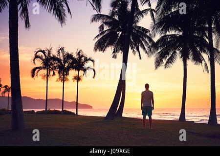 L'uomo guarda incredibile tramonto sulla spiaggia tropicale. Isola del Borneo, Malaysia. Foto Stock