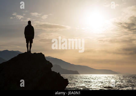 Escursionista o runner silhouette backpacker, un uomo in cerca di ispirazione paesaggio oceano e isole sul picco di montagna. Uomo realizzato celebrare la bella Foto Stock