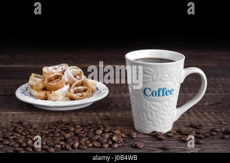 Tazza da caffè, refried fagioli e i cookie in zucchero a velo in background. Chiave di basso, il fuoco selettivo. Foto Stock