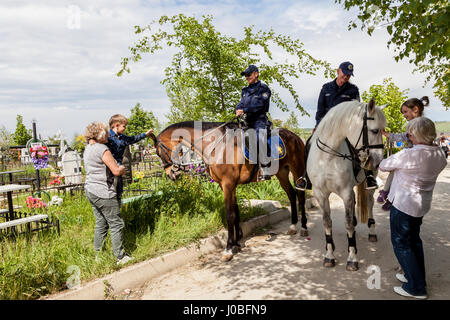 CHISINAU, REPUBBLICA MOLDOVA: polizia montata pattugliano la zona, fermandosi a lasciare che i bambini la corsa di cavalli. Visitatori in Europa il più grande cimitero sono stati innestati spezzando il pane con il morto. Ciò che potrebbe sembrare morboso è infatti una pratica tradizionale a Chisinau, in Moldavia. Le immagini mostrano le orde di persone che hanno amato-quelli sepolti in questo cimitero spooky impostazione e godendo di pic-nic intorno le tombe per commemorare il defunto in modo spettacolare. Mentre alcuni giovani da questo cristiano ortodosso di comunità può essere visto nonchalantly giocando sui loro telefoni. Il paesaggio tentacolare copre due milioni di squ Foto Stock