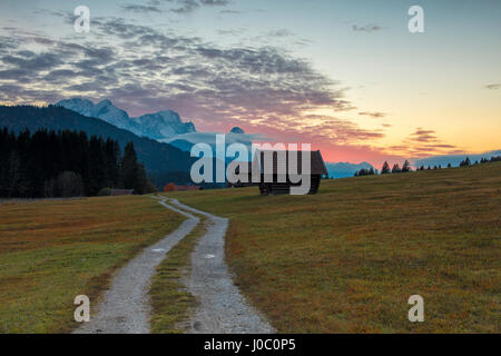 Tramonto sulle capanne in legno e prati con le Alpi in background, Geroldsee, Krun, Garmisch Partenkirchen, Alta Baviera, Germania Foto Stock