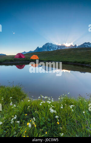 Tende da campeggio nel verde dei prati circondati da fiori e lago alpino, Mont De La Saxe, Courmayeur, in Valle d'Aosta, Italia Foto Stock