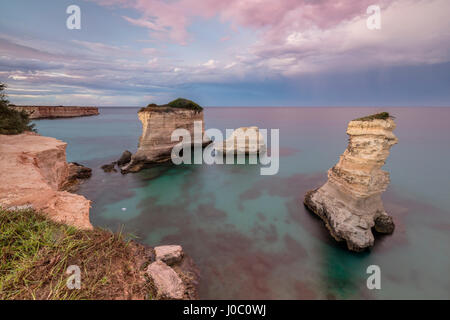 Rosa tramonto telai scogliere noto come Faraglioni di Sant'Andrea e il mare turchese, in provincia di Lecce, Puglia, Italia Foto Stock