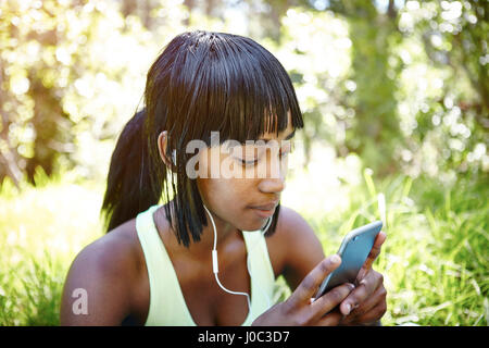 Giovane donna in ambiente rurale, utilizzando lo smartphone, indossa gli auricolari Foto Stock