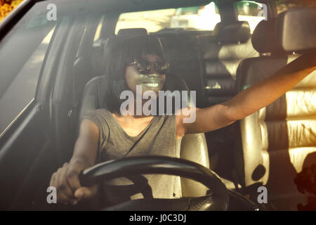 Giovane donna di regolazione dello specchietto retrovisore in auto, vista attraverso il vetro per auto Foto Stock