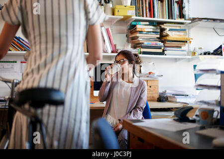 Donna in office di bere il caffè in chat a un collega Foto Stock