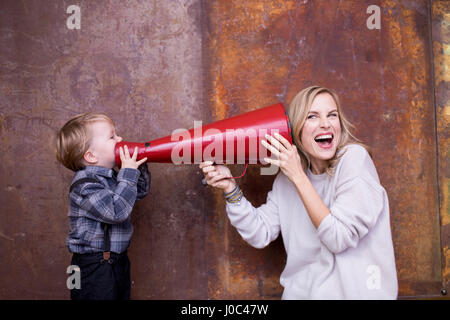 Giovane ragazzo parla nel megafono, donna holding megafono al suo orecchio Foto Stock