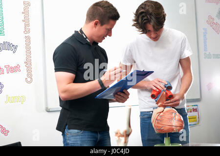 Studente maschio modello di tenuta valvole cardiache, essendo valutato dal tutor in classe di biologia Foto Stock