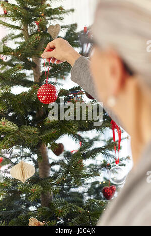 Senior donna mettendo ninnolo su albero di natale Foto Stock