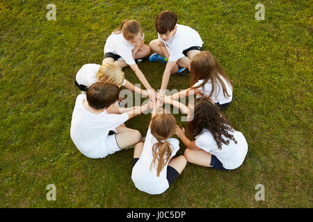 Vista aerea del ragazzo e ragazza sport team seduti su erba in cerchio sul campo da gioco Foto Stock