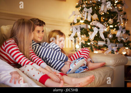 Ragazzo e ragazza a strisce in pigiama sul divano a natale Foto Stock