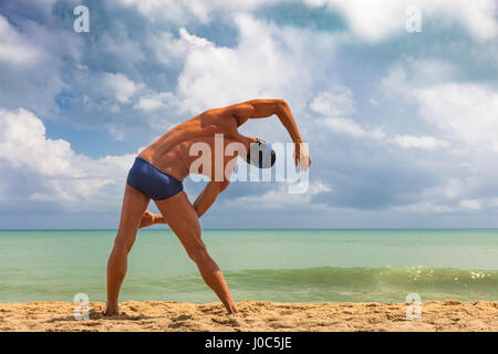 Vista posteriore del maschio muscolare nuotatore sulla spiaggia di piegarsi lateralmente Foto Stock