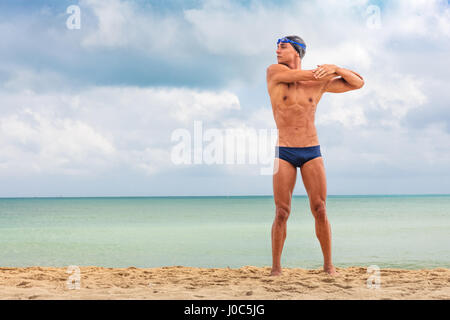 Maschio muscolare nuotatore permanente sulla spiaggia in fase di riscaldamento Foto Stock