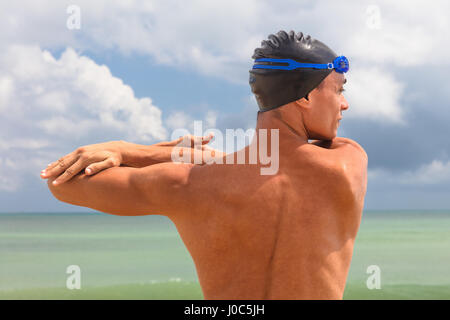 Vista posteriore del maschio muscolare nuotatore sulla spiaggia in fase di riscaldamento Foto Stock