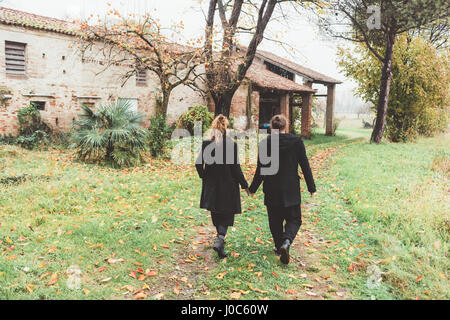 Vista posteriore del giovane passeggiando da vecchi edifici agricoli Foto Stock