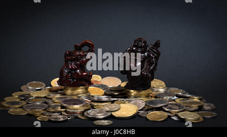 Statuine seduto su una grande pila di monete di portare buona fortuna Foto Stock