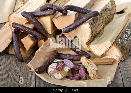 Tipico affumicato scuro e aria salsiccia secca da Alto Adige su registri con rami di ginepro, cosiddetto kaminwurz Foto Stock