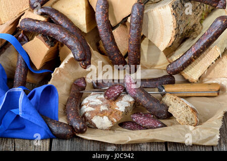 Tipico affumicato scuro e aria salsiccia secca da Alto Adige su registri con rami di ginepro, cosiddetto kaminwurz Foto Stock