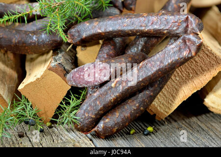 Tipico affumicato scuro e aria salsiccia secca da Alto Adige su registri con rami di ginepro, cosiddetto kaminwurz Foto Stock