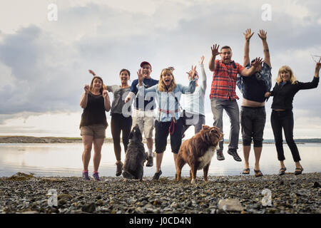 Ritratto di famiglia per adulti con cani salto sulla spiaggia di ciottoli, Maine, Stati Uniti d'America Foto Stock