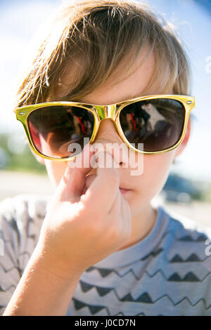 Ritratto di ragazzo in golden occhiali da sole la raccolta il suo naso Foto Stock