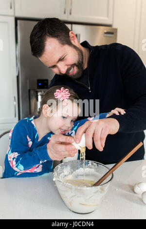 Metà uomo adulto e figlia di uovo di cracking nel recipiente di miscelazione insieme al banco di cucina Foto Stock