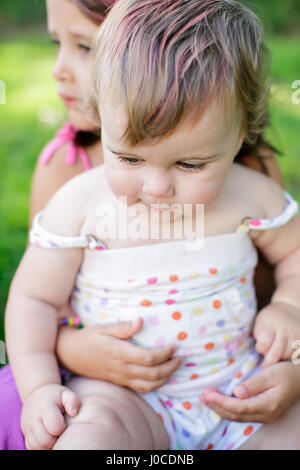 Close up toddler femmina seduto sulla ragazza in ginocchio in giardino Foto Stock