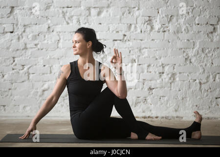 Yogi giovane donna attraente in Ardha Matsyendrasana pongono, bianco Foto Stock