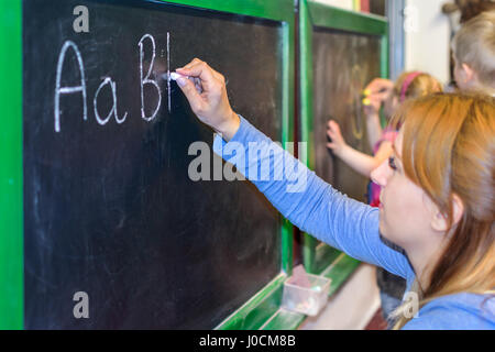 Insegnante mostra ai bambini come scrivere le lettere dell'alfabeto sulla lavagna a scuola Foto Stock