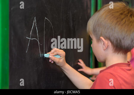 Little Boy imparare a scrivere su una lavagna nella scuola materna o la classe Foto Stock