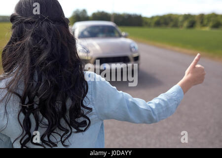 Donna autostop e arresto di auto con pollice in alto Foto Stock