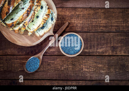 Semi di papavero in una ciotola di legno e un cucchiaio su una superficie di colore marrone, una vista superiore Foto Stock