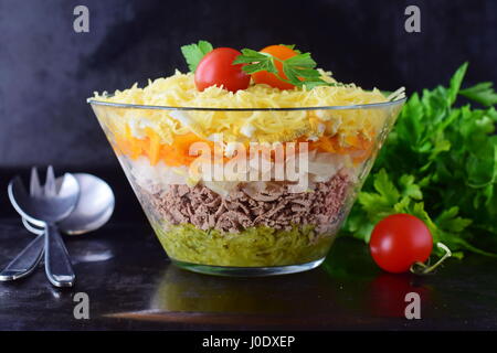 Insalata con fegato di pollo in strati con sottaceti,carota lessata, l'uovo, il formaggio in una ciotola di vetro su di un nero sfondo astratto. vista dall'alto. cibo sano concetto. Foto Stock