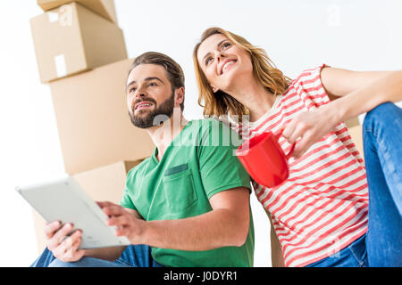 Coppia giovane con tavoletta digitale e di bere il tè tra le scatole di cartone Foto Stock
