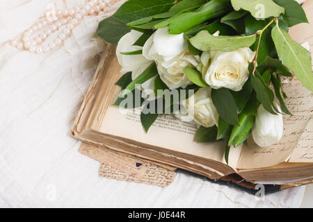 Vecchio libro aperto con fiori di colore bianco vicino sul romantico sfondo pizzo Foto Stock