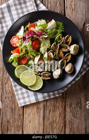 Di vongole fresche con calce e verdi e insalata di mix di close-up su una piastra. Vista verticale da sopra Foto Stock
