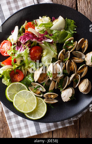 Le vongole con verdi e insalata fresca di close-up su una piastra su un tavolo. Vista verticale da sopra Foto Stock