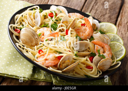 Deliziosi spaghetti alle vongole, gamberi e verdi close-up su una piastra orizzontale. Foto Stock