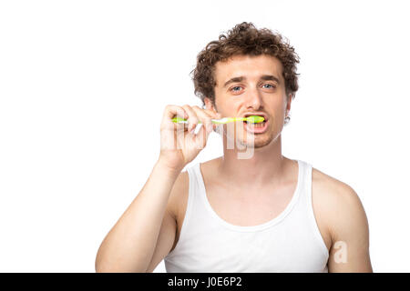 Curly divertente gli uomini con la canottiera bianca spazzolando i suoi denti con cura, isolato su bianco Foto Stock