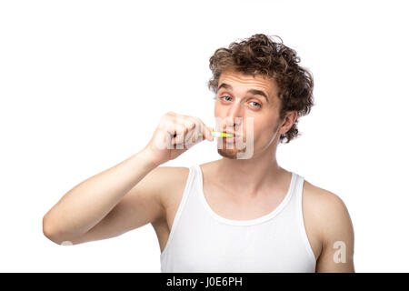 Curly divertente gli uomini con la canottiera bianca spazzolando i suoi denti con cura, isolato su bianco Foto Stock