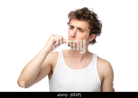 Curly divertente gli uomini con la canottiera bianca spazzolando i suoi denti con cura, isolato su bianco Foto Stock