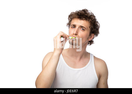 Curly divertente gli uomini con la canottiera bianca spazzolando i suoi denti con cura, isolato su bianco Foto Stock