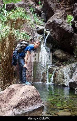 L'uomo escursionista con zaino in piedi vicino all'acqua di cascata. Percorso escursionistico in Masca gorge. Tenerife, Canarie, Spagna, Europa Foto Stock