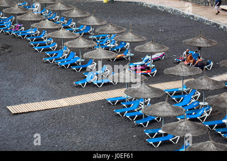 CALLAO SALVAJE, Tenerife, Canarie, Spagna-CIRCA gen, 2016: Blu lettini e ombrelloni di paglia sono su Playa de Ajabo beach. Oceano Atlantico. Pubblico di piccole dimensioni Foto Stock