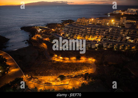 Vista aerea a edifici di alberghi con illuminazione notturna. L'isola di Gomera con tramonto sull'oceano Atlantico. Playa Paraiso Beach, Tenerife, Canarie, Foto Stock