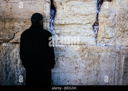 Un ebreo ortodosso mette la testa stretta contro il Muro del Pianto mentre dicendo preghiere. Le incrinature del muro sono pieni di scivola di carte con scritto il pra Foto Stock