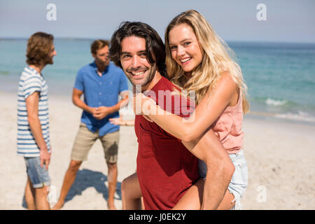 Ritratto di felice ragazzo piggybacking ragazza da amici in spiaggia Foto Stock