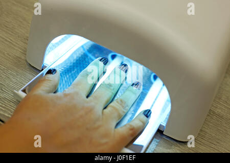 Primo piano della mano di una donna dentro una lampada UV, indurendo il suo recentemente applicato su gel di smalto per unghie in un salone Foto Stock